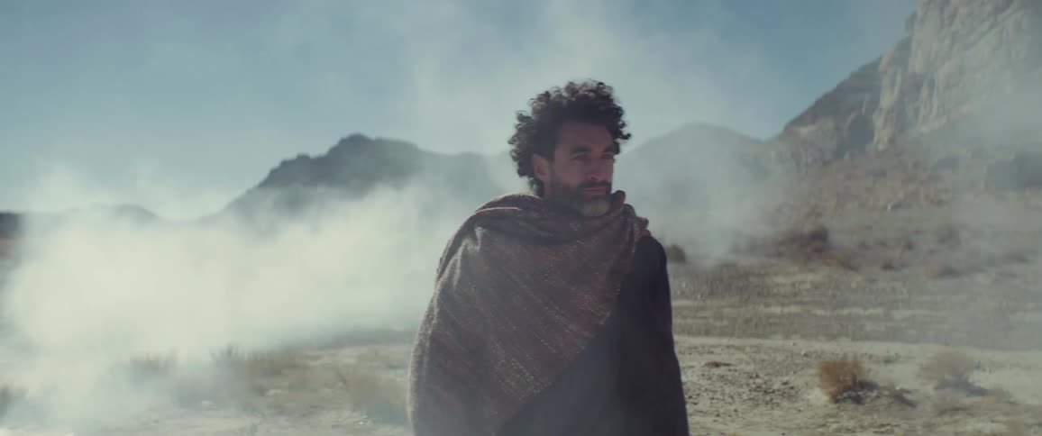 A man walks across a barren mountainous landscape