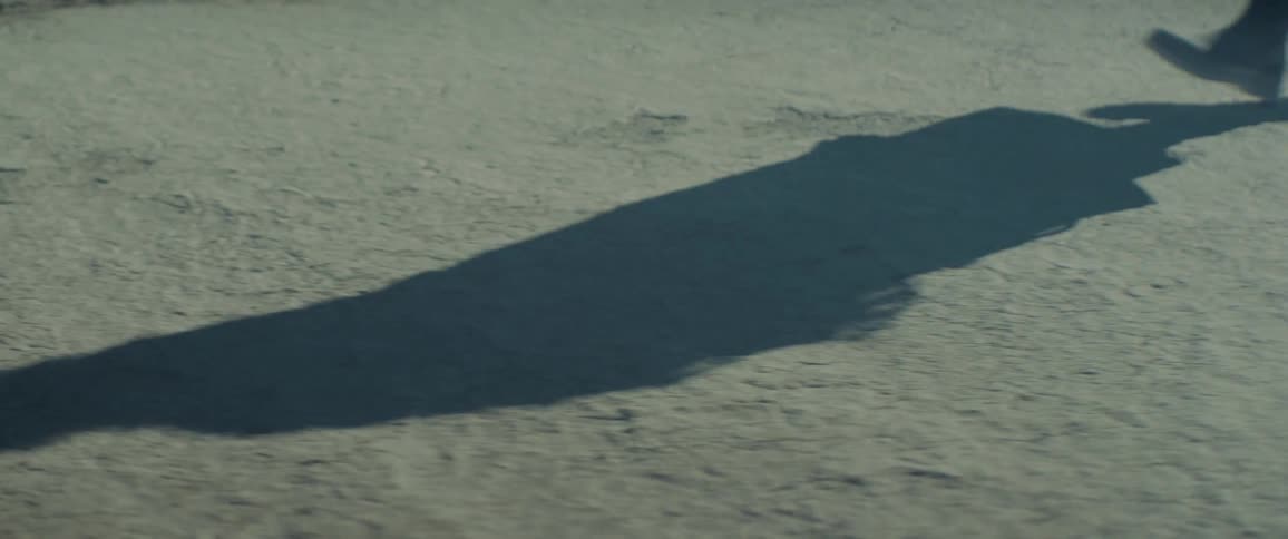 A person is casting a long shadow as they walk across sand