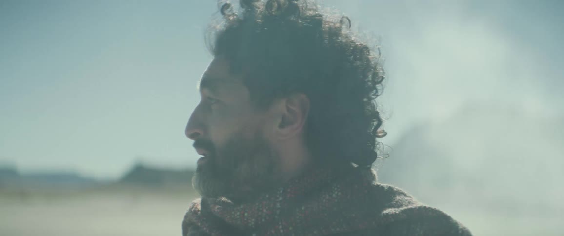 A man is standing in a desert looking all around while sand blows