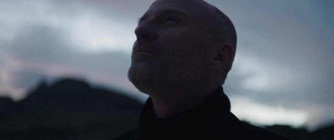 Middle aged man with black turtleneck sweater looks around in the desert at dusk