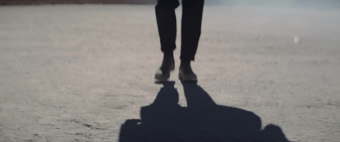 A mans shadow precedes him as he walks on cracked dry ground