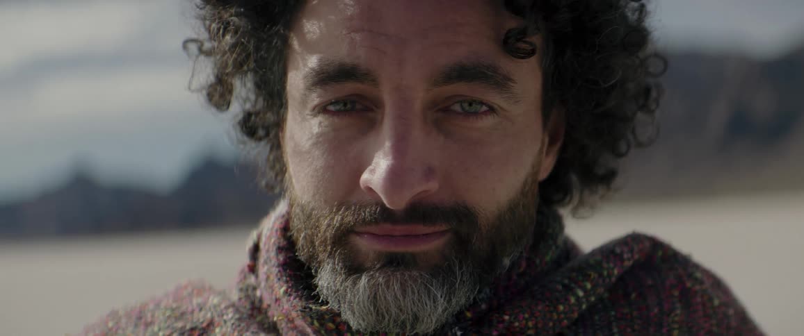 A man stands still with his face full of emotion with mountains as a backdrop