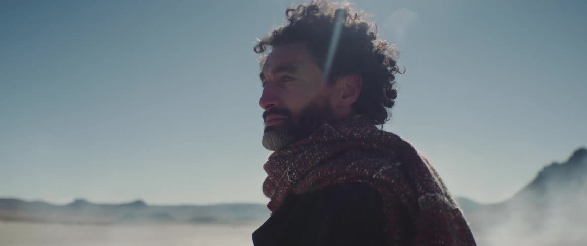 A man looks around a desert area as sand blows all around him