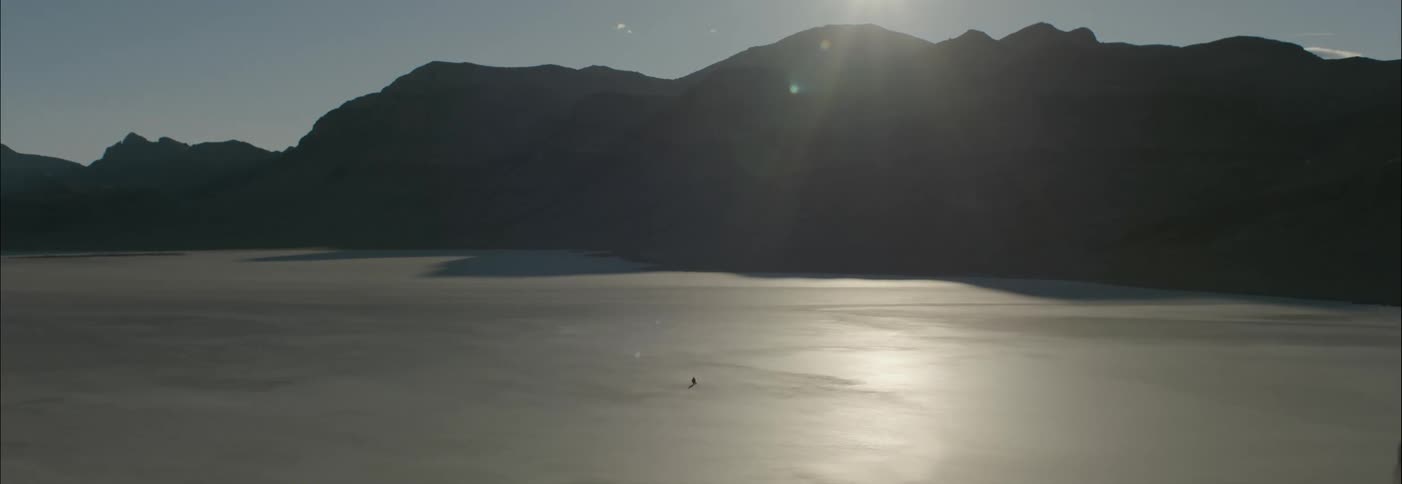 A lone figure in a vast barren landscape with the sun shining down