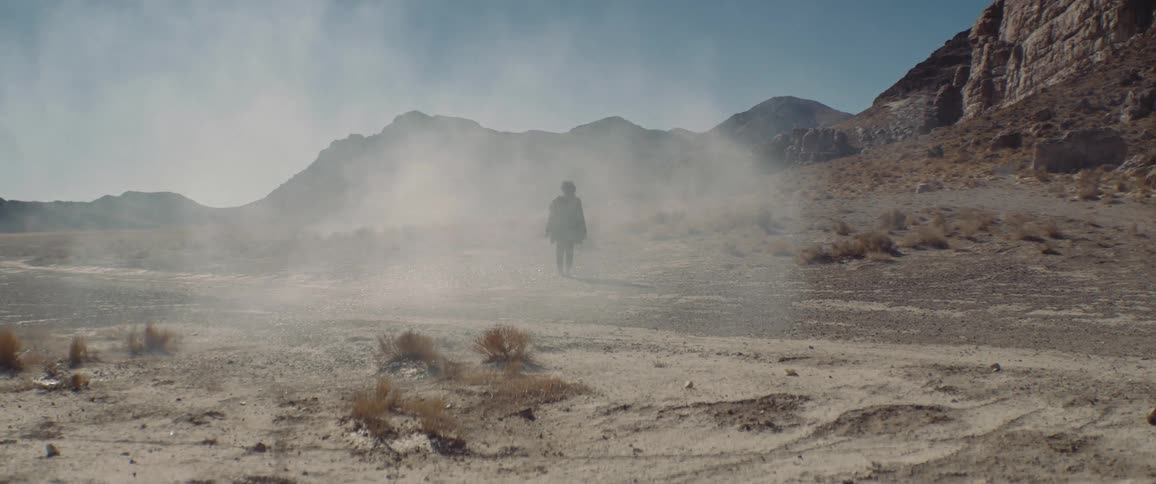 A man looks around at his surroundings while walking through arid badlands during the day