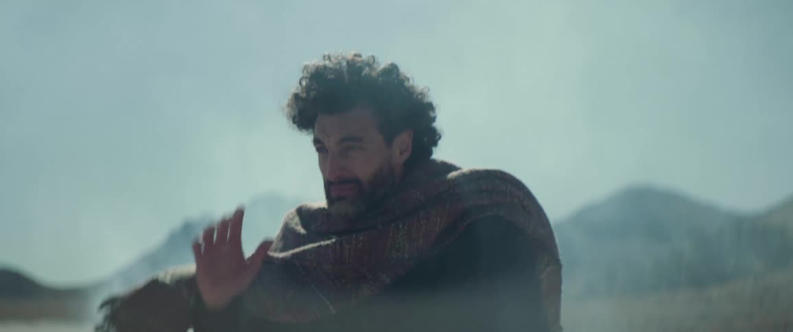 A man sitting on the ground looking defeated in the elements gets up and starts walking