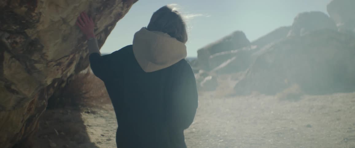Elderly woman walks around corner of rock wall as smoke flows through air