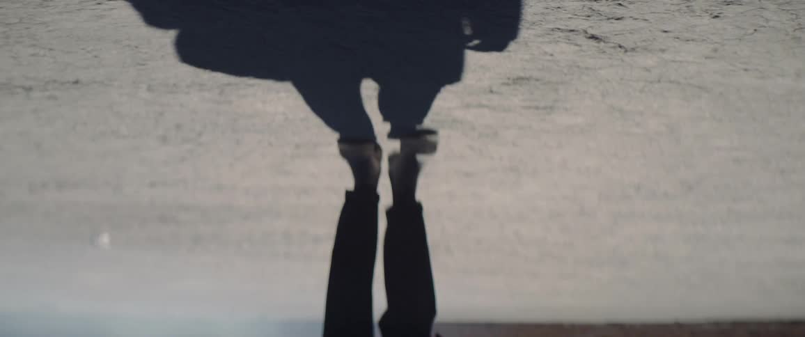 A man casts a shadow on the cracked soil as he walks through the badlands during the day