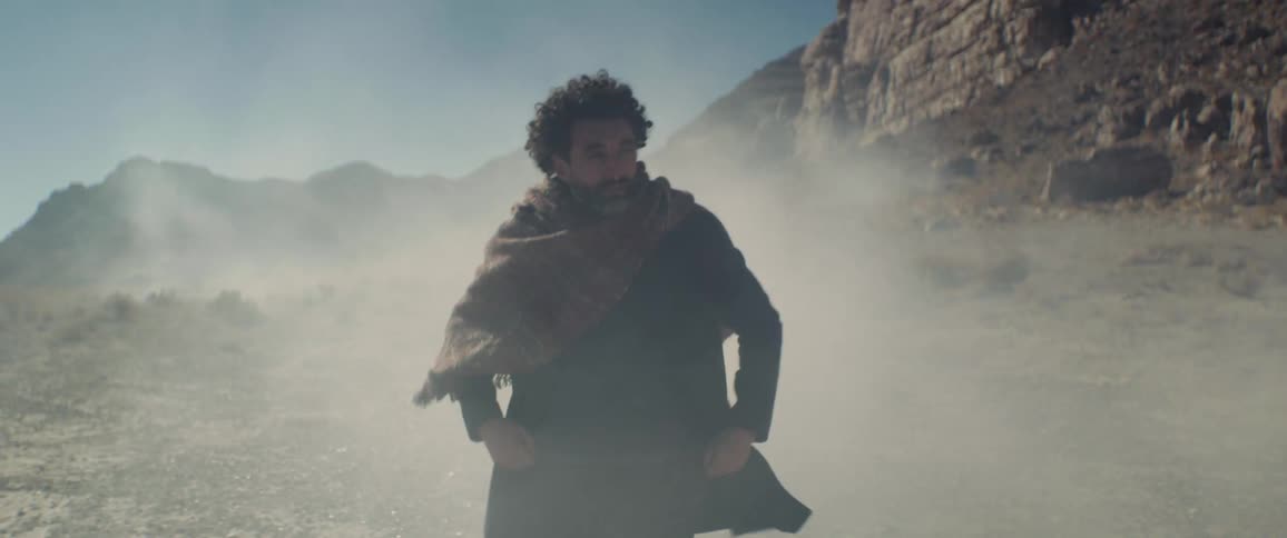 A man casually walks through clouds of dust in the badlands during the day