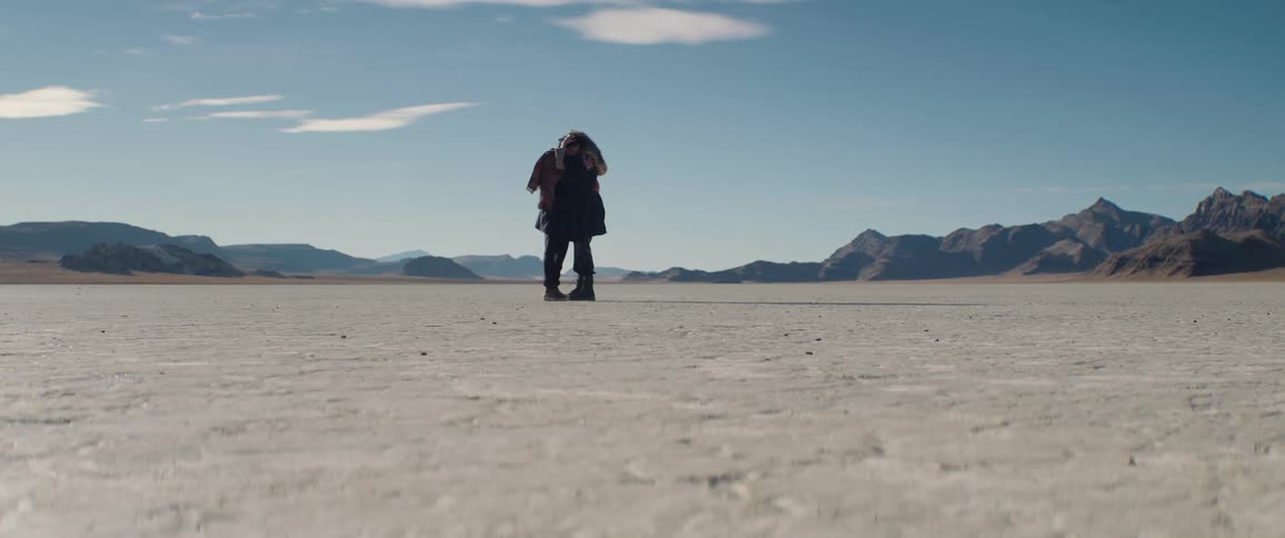 A man and a woman in a desert hug one another