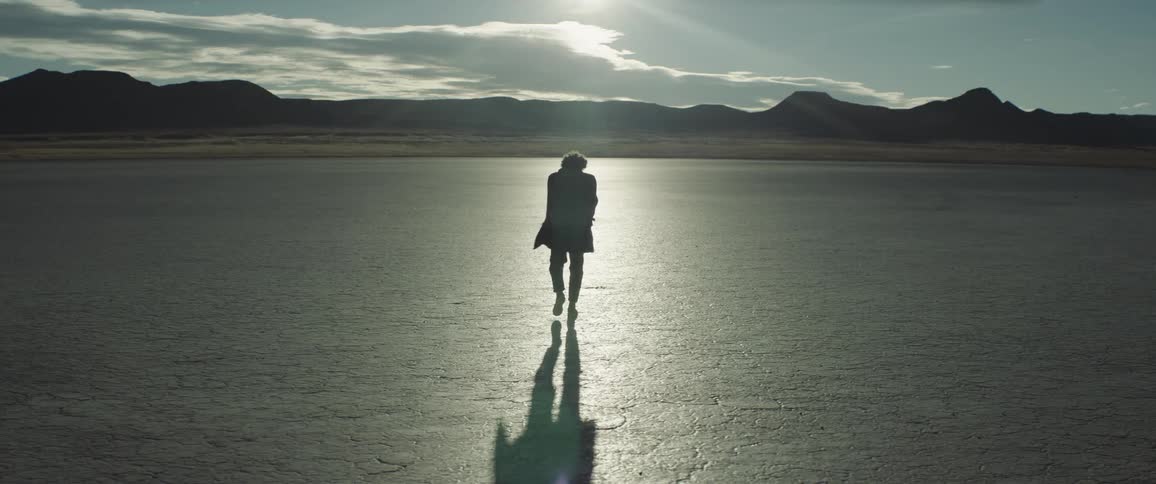 A man walks across a desert area and looks around