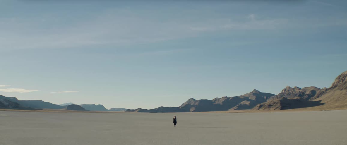 A woman is walking in a desert surrounded by mountains