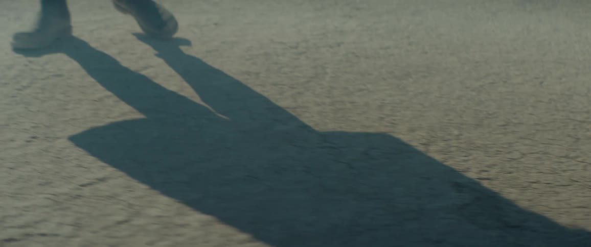 The legs and shadow of person taking stumbling steps on dry cracked ground
