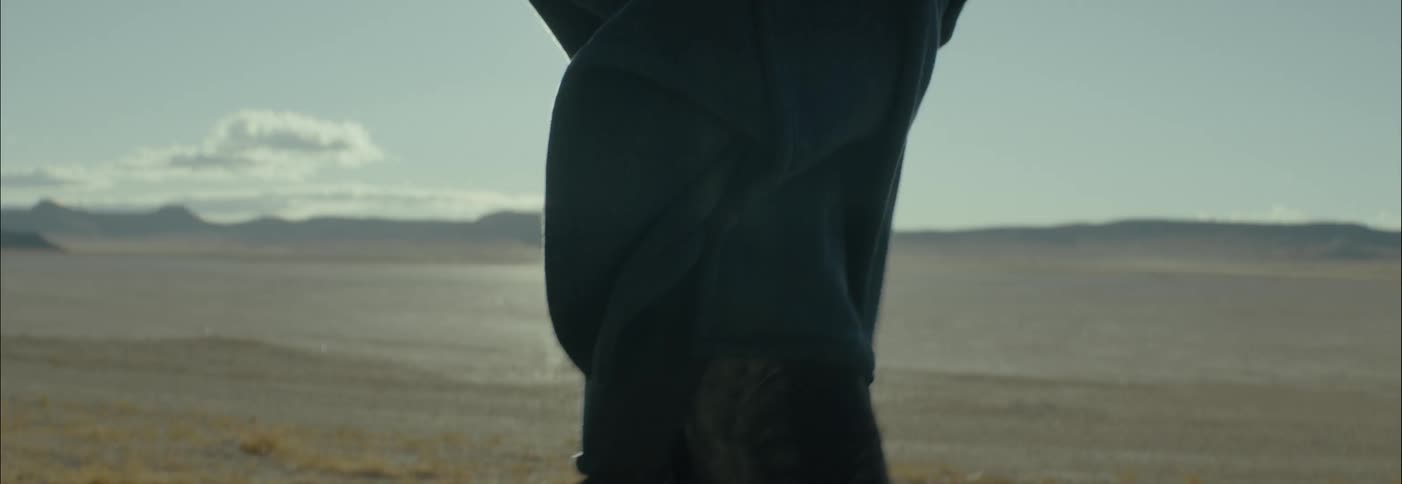 A woman holds onto her coat as she walks across a desert