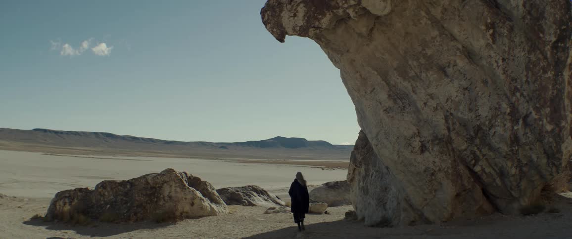 A woman walks in the shadow of a large rock formation in the badlands during the day