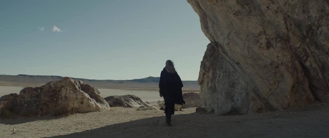 A woman walks next to large rock formations toward a desert