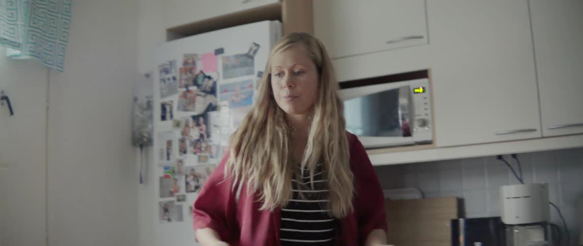 A blonde woman clearing items from a kitchen table while performing daily household chores.
