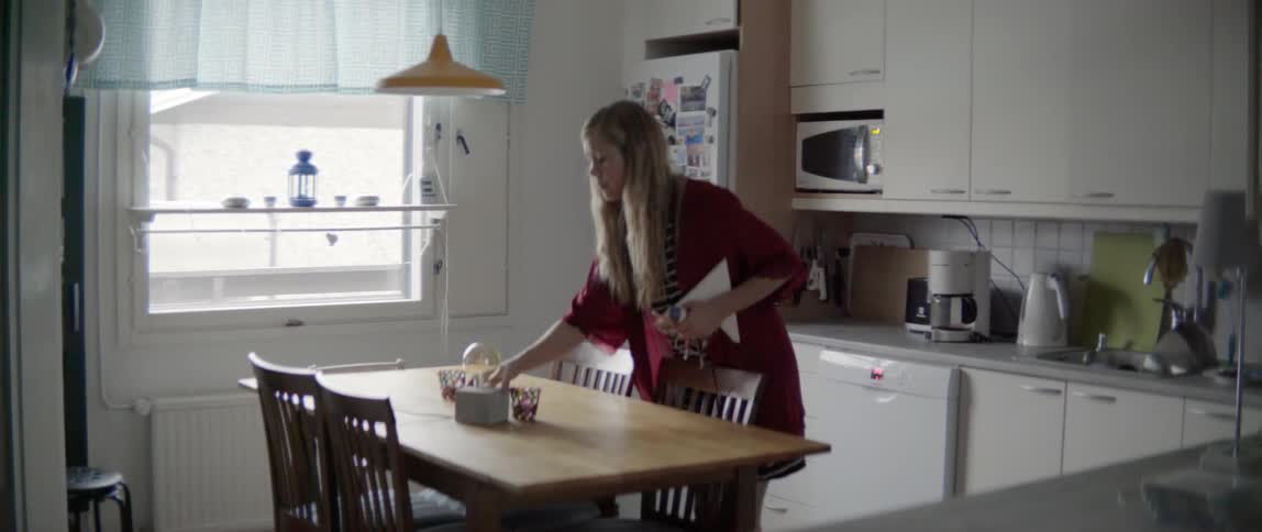 A woman clears items from a kitchen table during the morning
