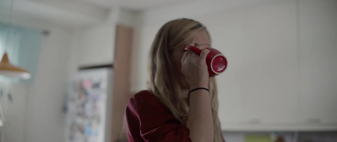 A woman takes a drink from a mug while standing in a kitchen