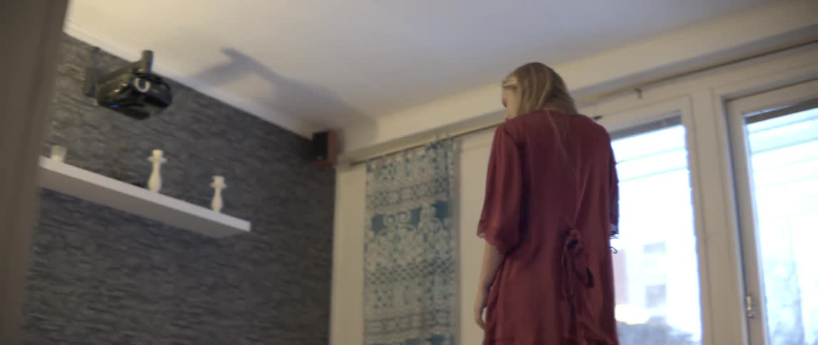 A woman walks into a messy living room and puts a mug down