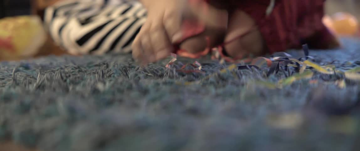 A woman tidies a messy blue carpet by picking up small pieces of party litter.
