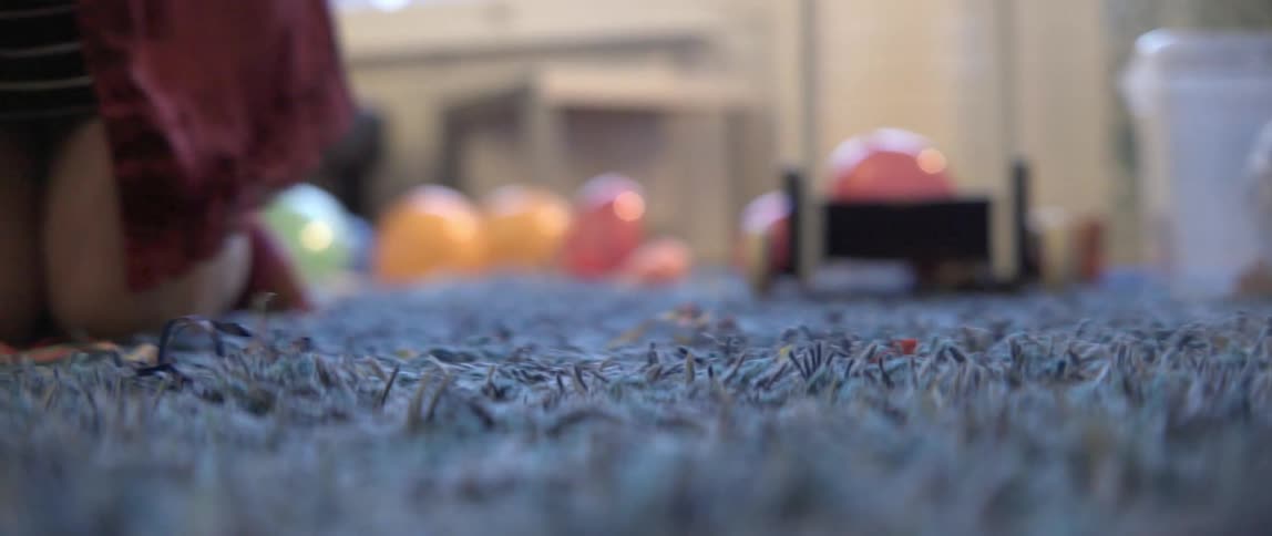 Person crawling on the floor while gathering party scraps and debris from a plush rug.
