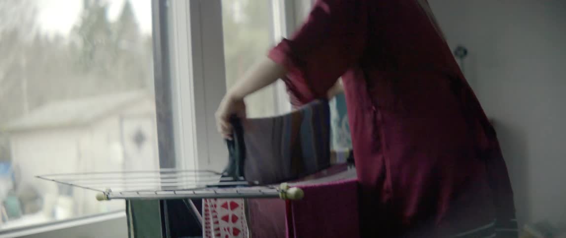 A woman is hanging clothes on a clothesline by the window