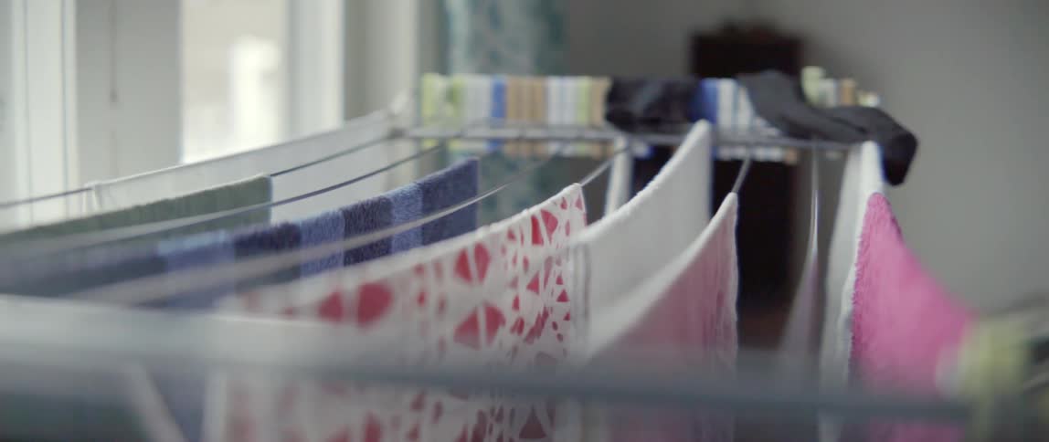 Young woman hanging garments on a metal drying rack during a domestic task.