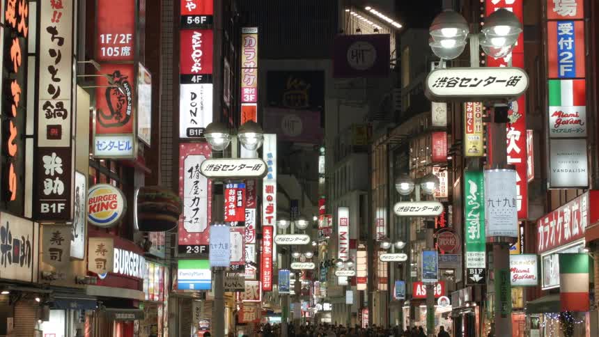 A busy city street has many lit signs on the shops
