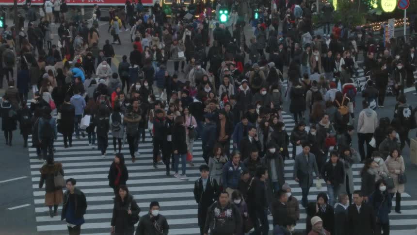 Large crowds of people travel across an intersection in a city