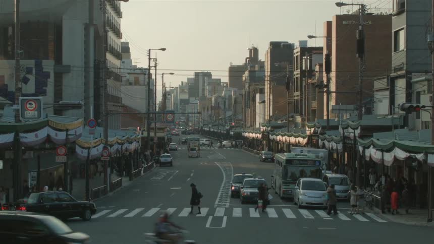 A busy city street has people crossing as cars are stopped at a traffic light