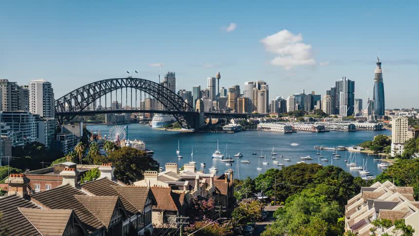 Boats traveling under the sydney harbor bridge with the city skyline behind on a bright sunny day
