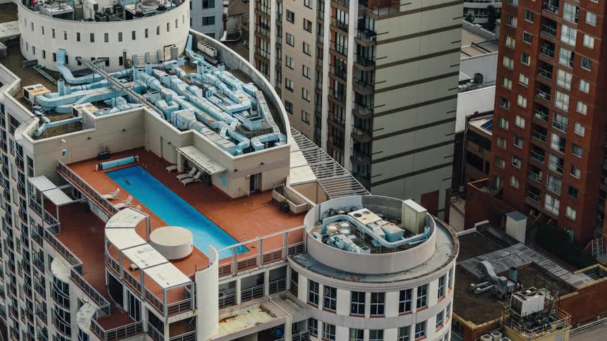 A swimmer swims back and forth in a rooftop pool in a city during the day