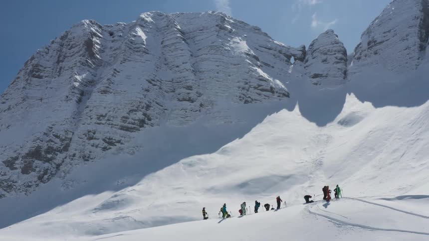 Skiing party stands on slope near cliff with clouds and contrail in the sky