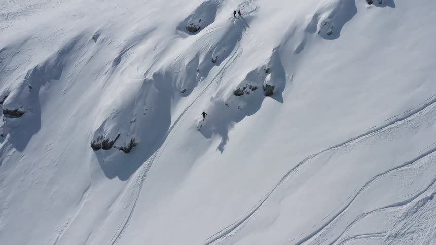 A skier descends a steep mountain slope during the day