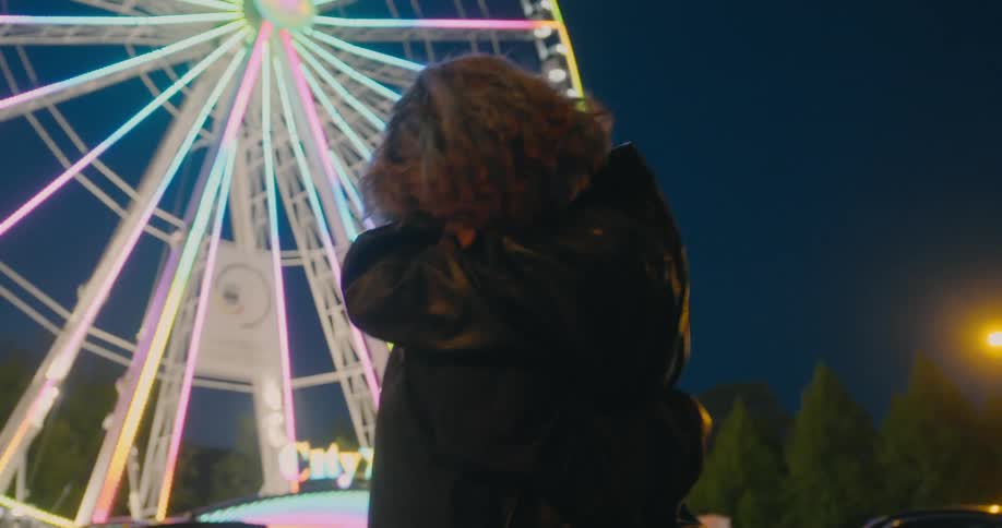 Happy woman hugging another person in front of a ferris wheel in a fun fair at night