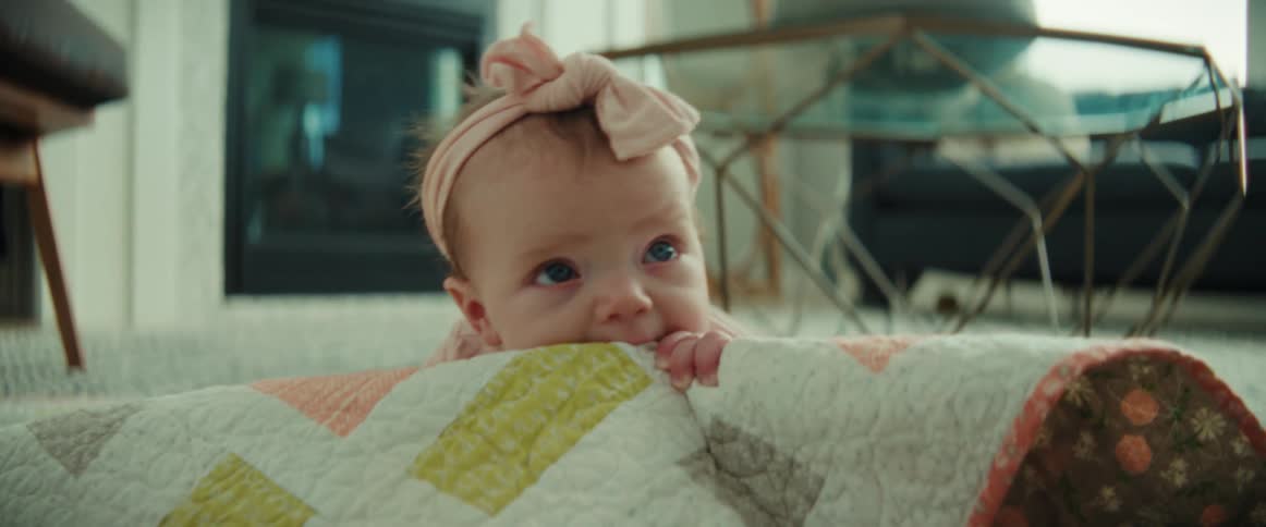 A female infant is crawling on a blanket indoors