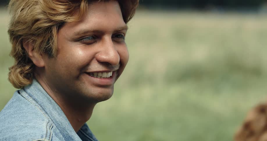 A man sits in a grassy field and smiles as he talks with a woman