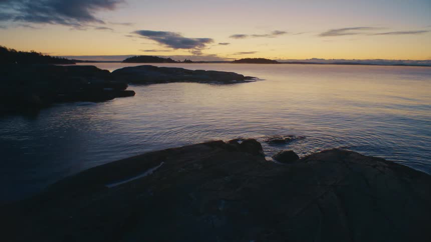 Water gently laps at the rocks and ripples at sunset