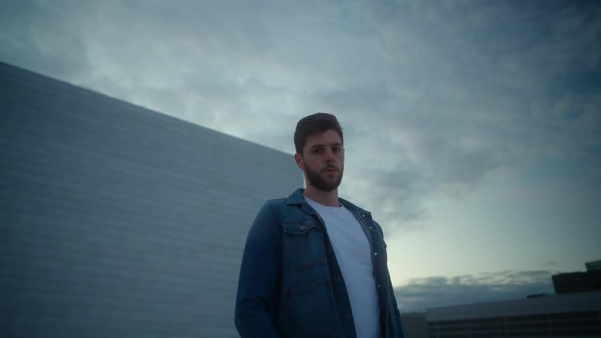 A man is standing outdoors by a building at dusk