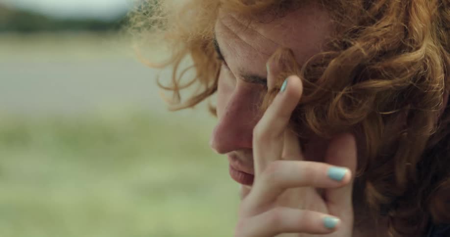 Male redhead sitting outdoors on windy day pushes his hair out of his face and smiles at another person