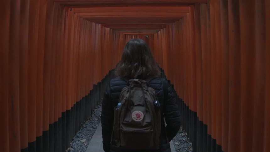A woman wearing a backpack walks down a long narrow corridor