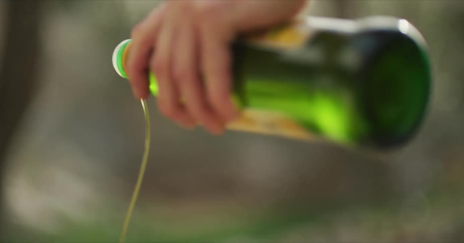 A person is pouring olive oil from a bottle outdoors