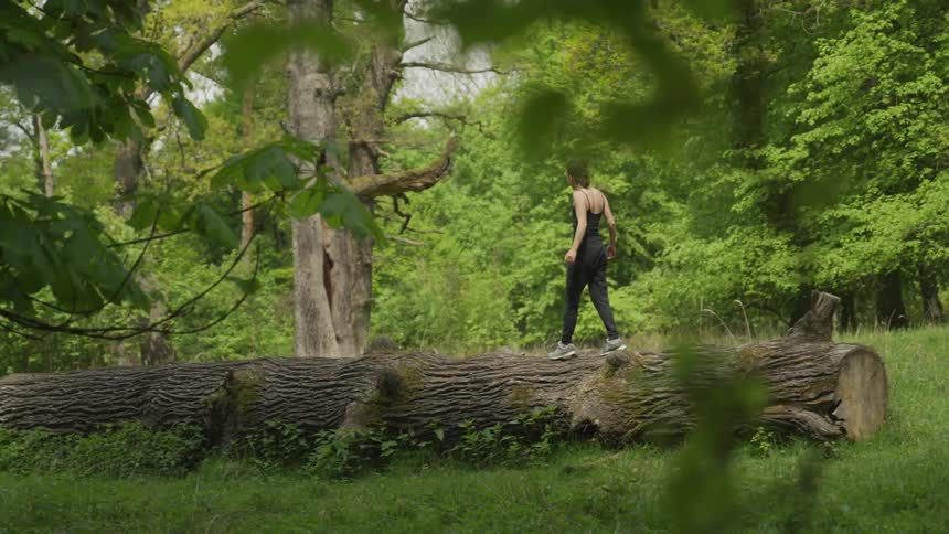 A woman is walking on a tree in the forest outdoors