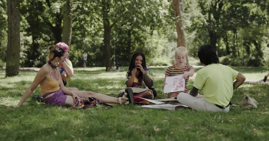 A group of friends are sitting at a park and making signs