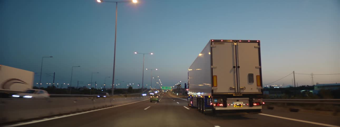 A semi truck travels on a highway among light traffic at dusk