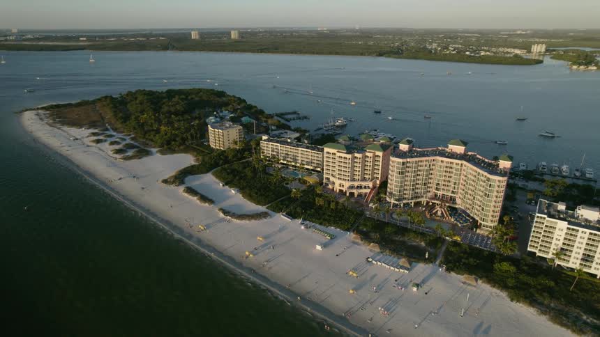 People move along beach on peninsula as boats sail through bay