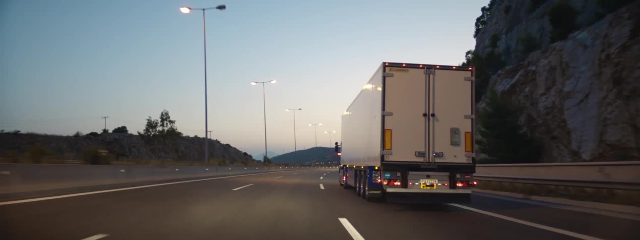 A shipping truck is driving on a highway at dusk