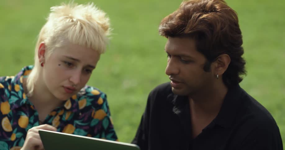 Woman and man discuss contents of laptopscreen outdoors on grass
