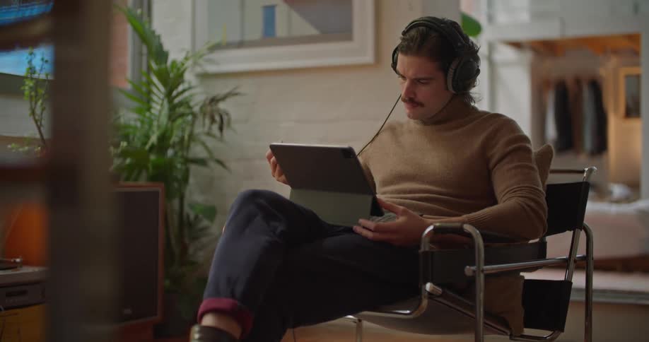 Man sits and listens to music while he uses stylus on tablet
